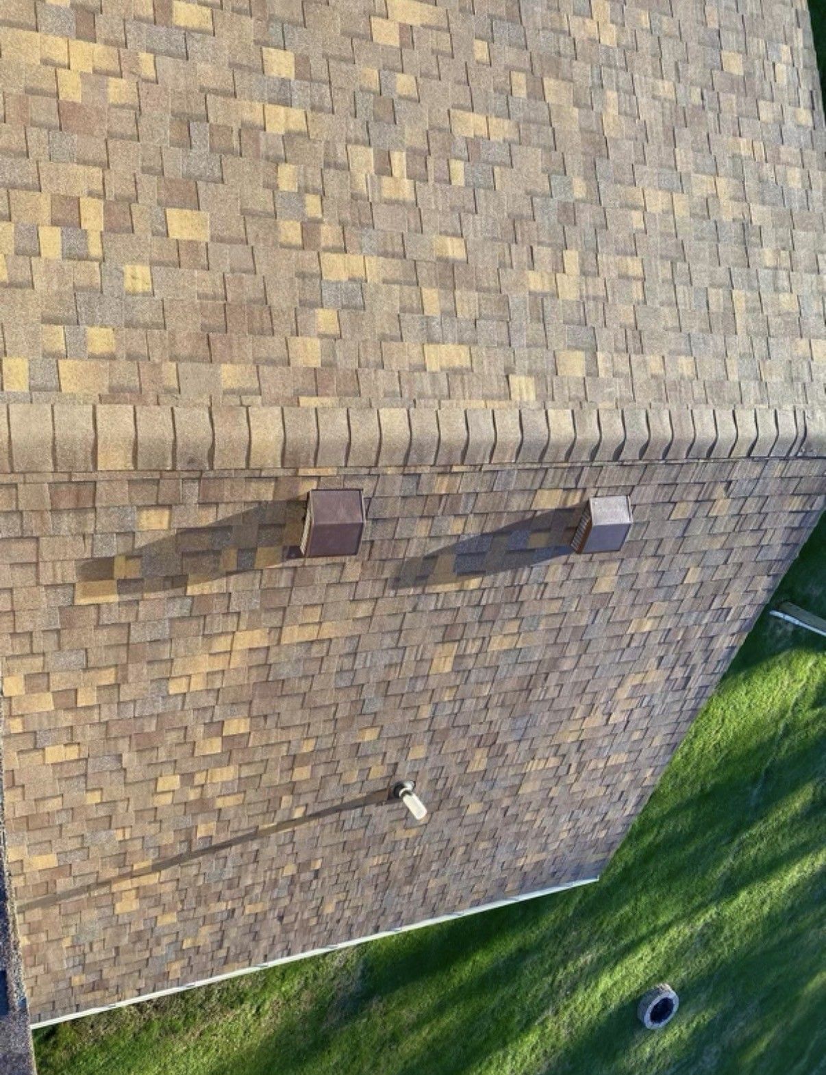Rooftop shingles with two vent pipes beside a grassy yard below