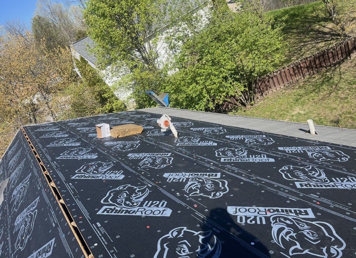 Roof deck under construction with black underlayment and rolls of roofing material outdoors
