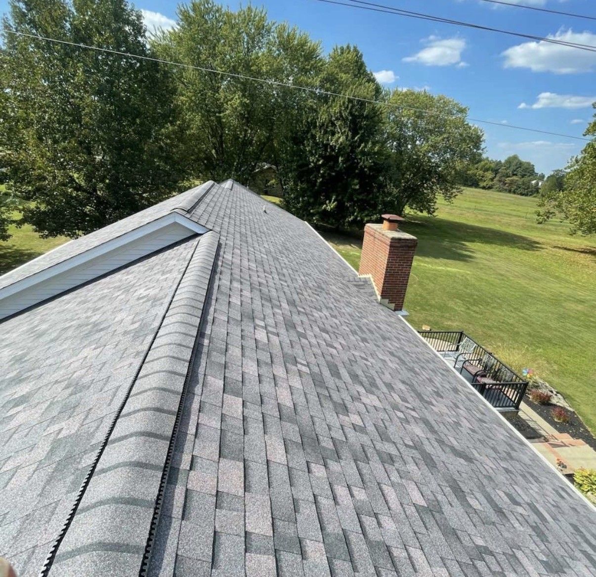 Gray shingled roof with chimney, viewed from the ridge above a green, wooded landscape