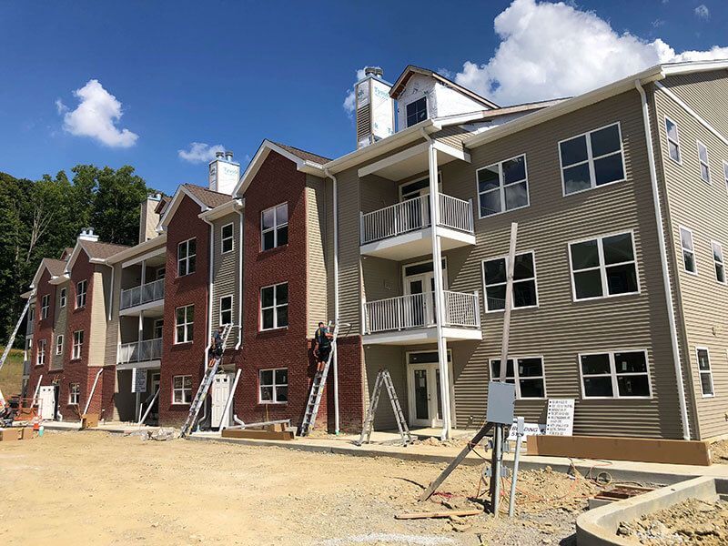 Row of unfinished apartment buildings with scaffolding and dirt ground under a blue sky