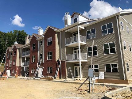 Row of unfinished apartment buildings with scaffolding and dirt ground under a blue sky