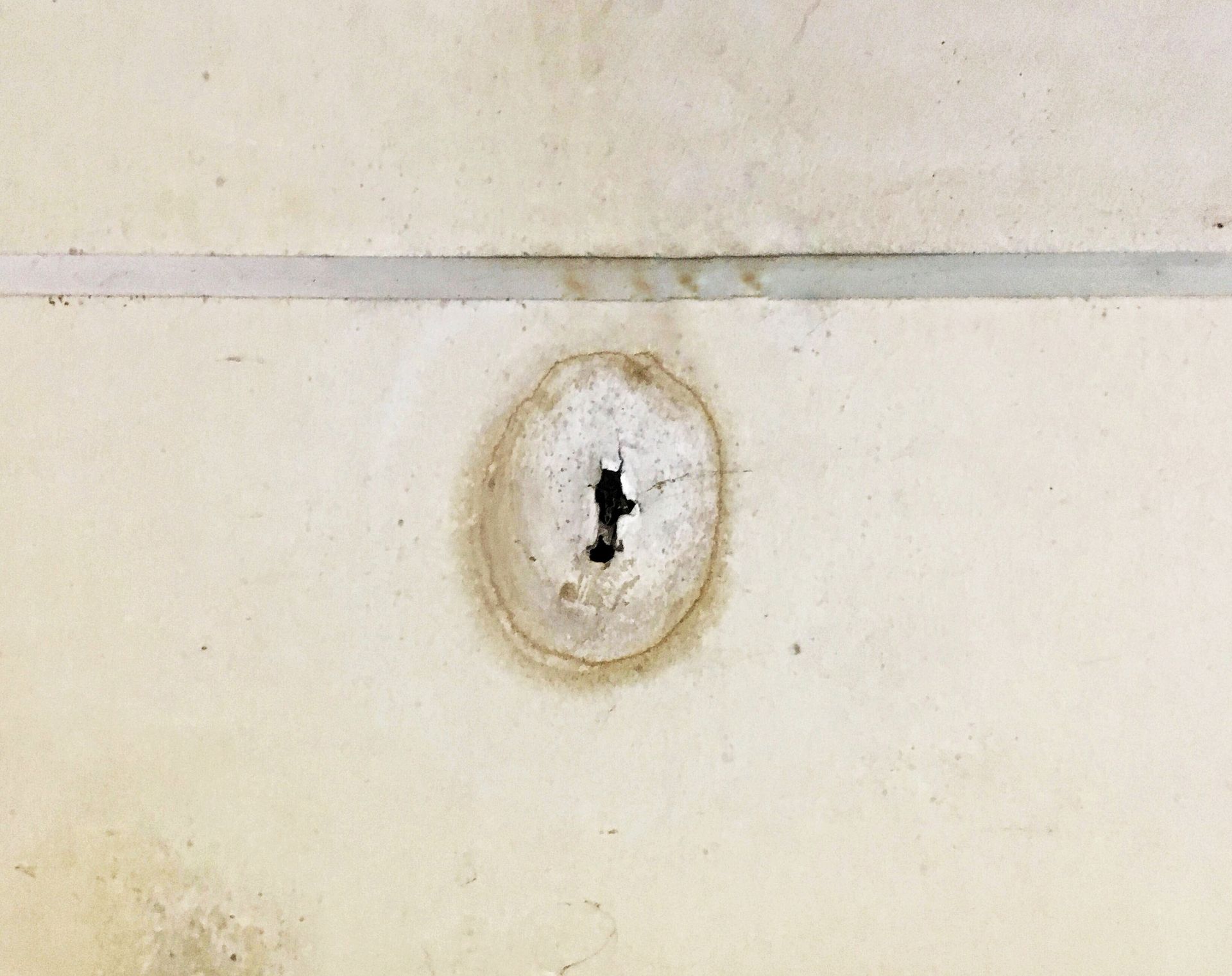 Close-up of a beige wall with a small circular stain and a dark keyhole-shaped mark in the center