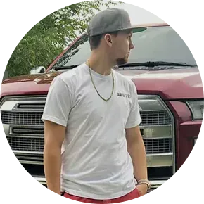 Man wearing a baseball cap and a white shirt stands next to a red truck, looking to the side.