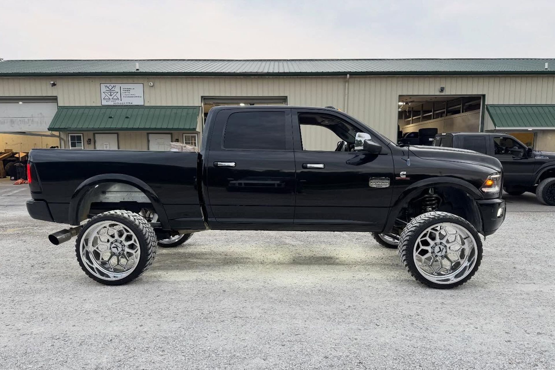 Black Ram truck with chrome wheels, lifted, parked outside a building.
