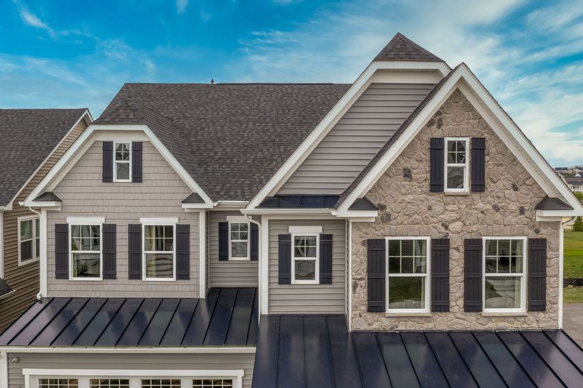 Multi-story home with gray siding, stone accents, and black shutters against a blue sky.
