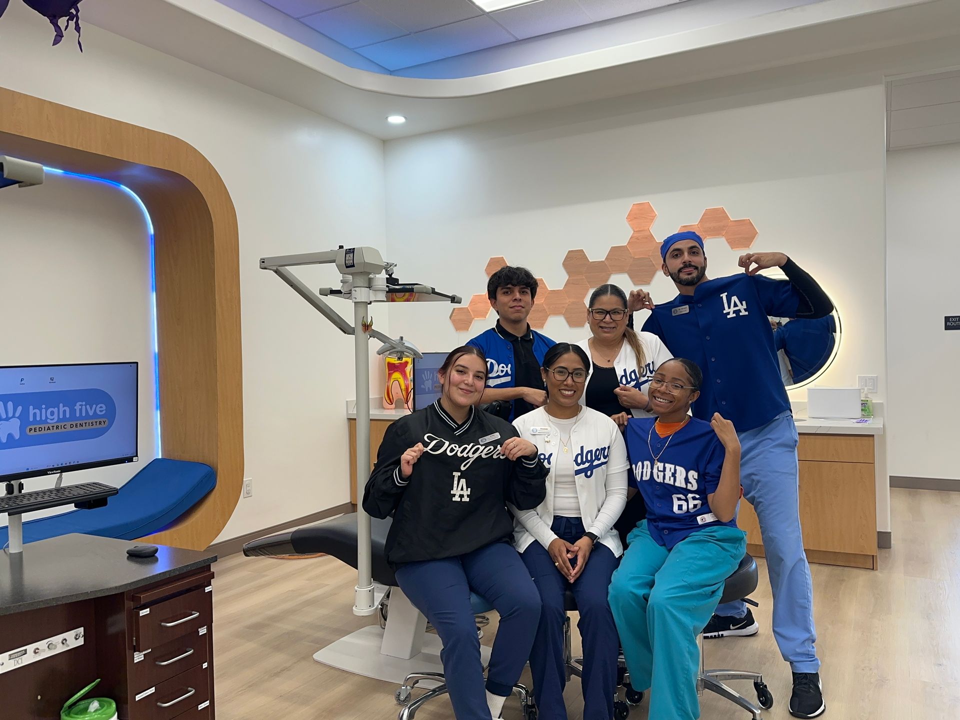 A group of six people posing in a dental office, wearing Dodgers-themed apparel and smiling for a photo.