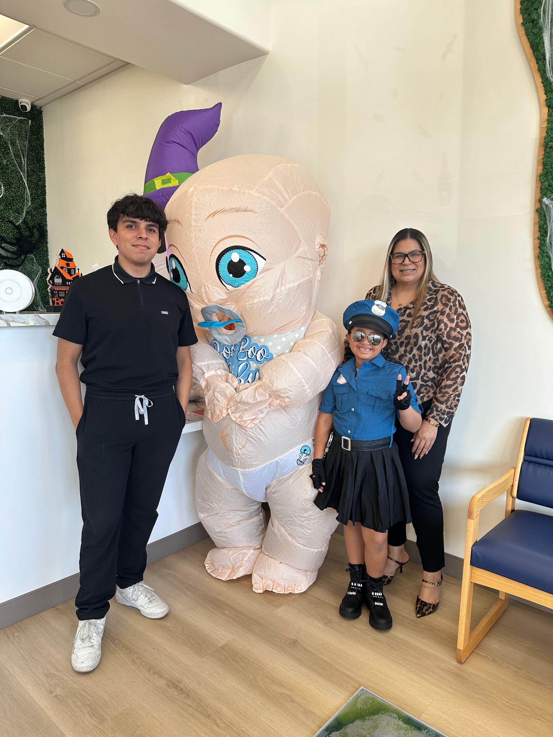 Four people pose for a photo: one in a large inflatable baby costume, and three others in casual and police costumes.