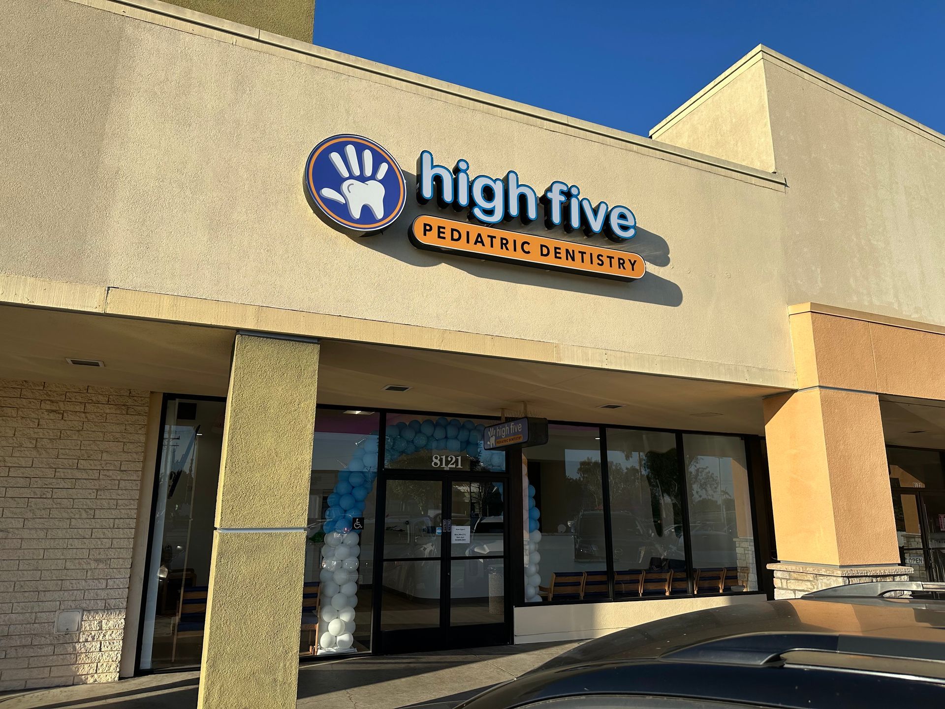 A storefront for High Five Pediatric Dentistry with a blue hand-shaped logo, orange text, and large glass windows.