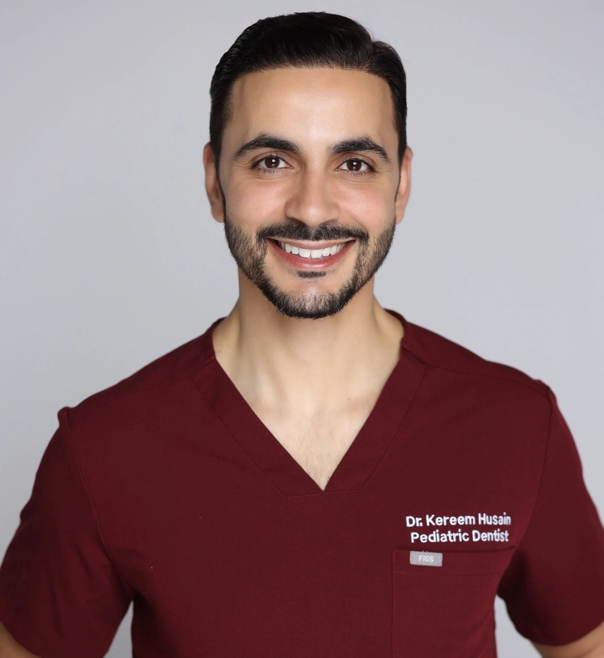 A person in a maroon scrub top smiling against a light gray background, with text on their chest reading 
