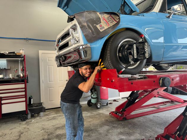 Man working under a raised blue race car in a garage on a red lift