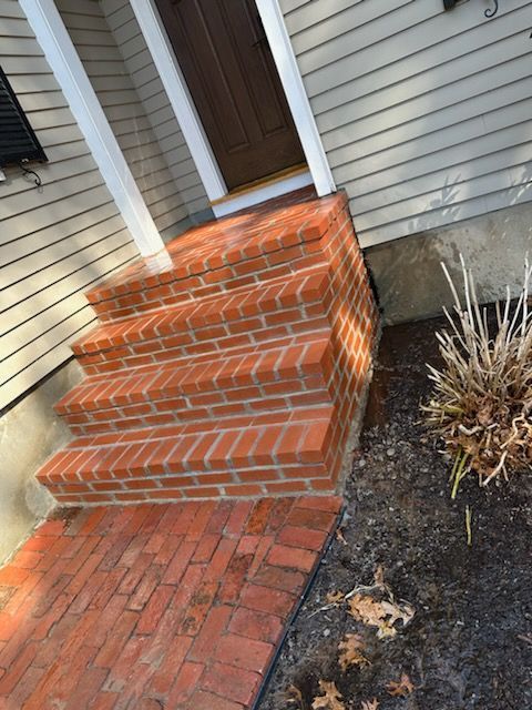 Brick front steps leading to a brown door beside gray siding and a small landscaped bed
