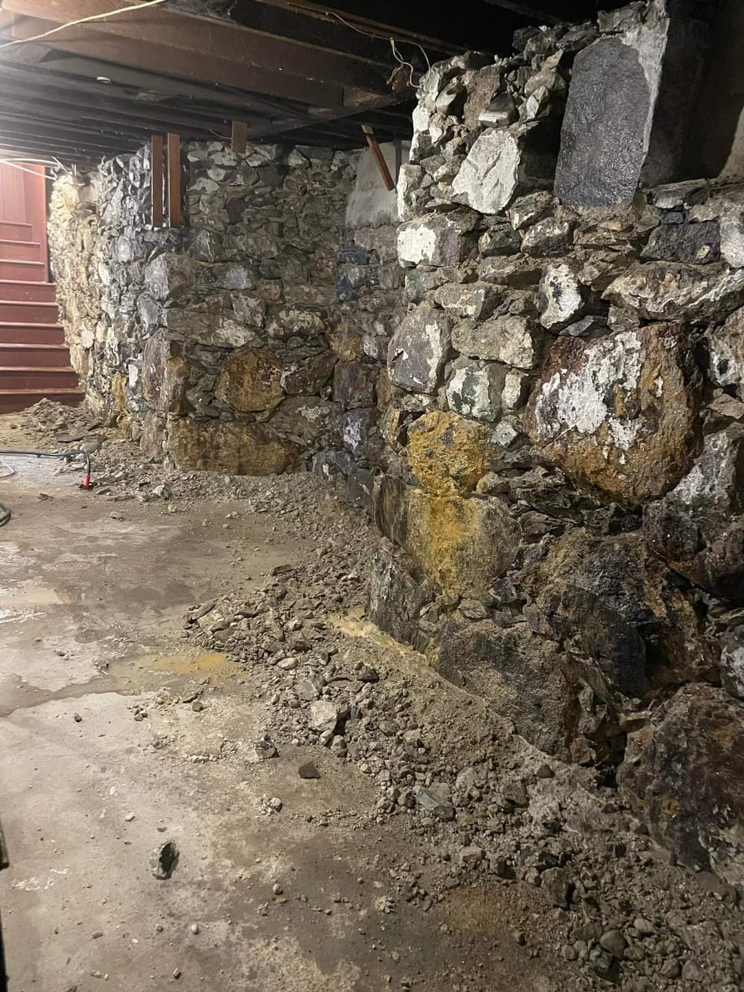 Rough stone basement wall with damp, crumbling mortar under a low wooden ceiling