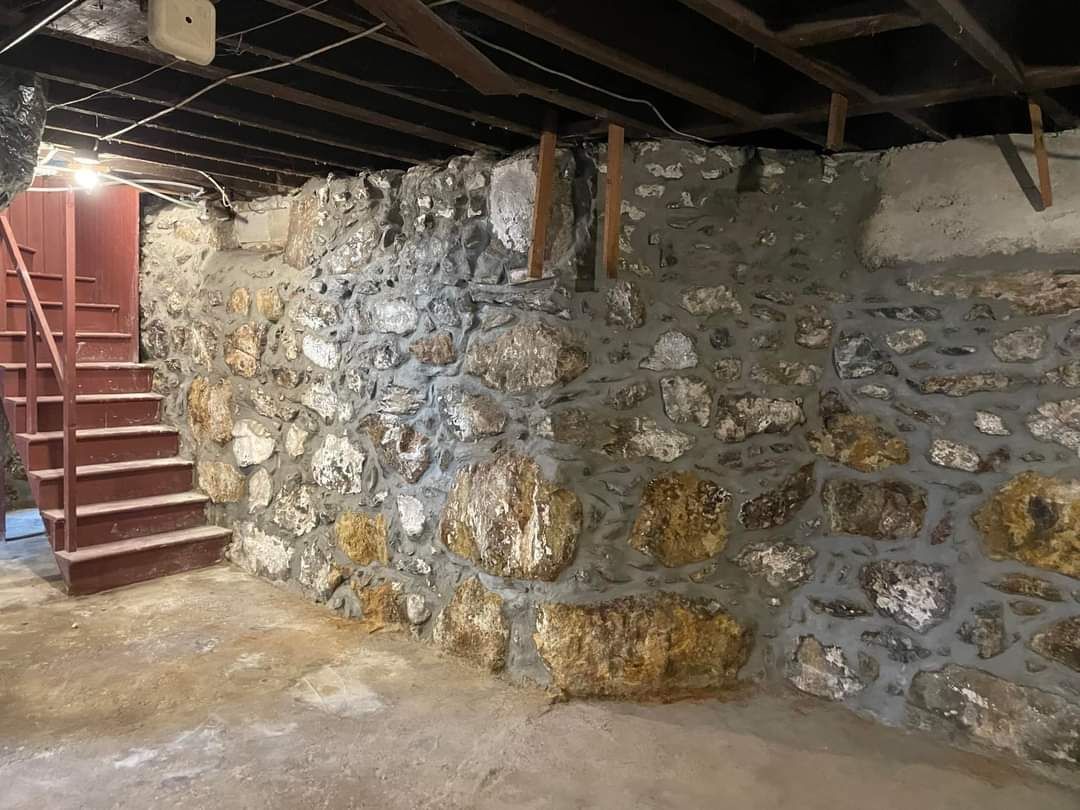 Stone basement with red stairs, exposed beams, and a rough concrete floor