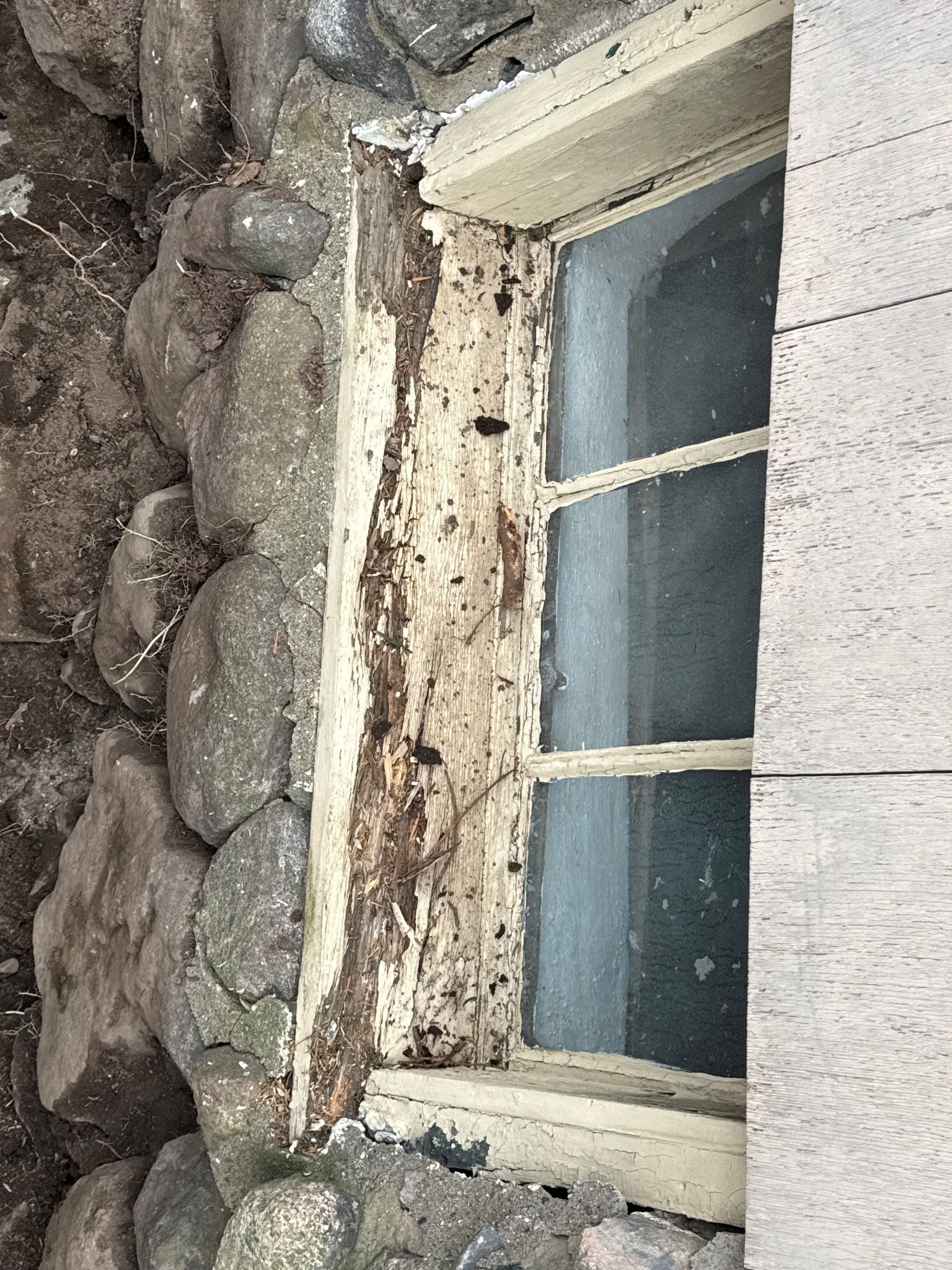 Close-up of a weathered window set in a stone wall, with peeling white trim and frosted glass.
