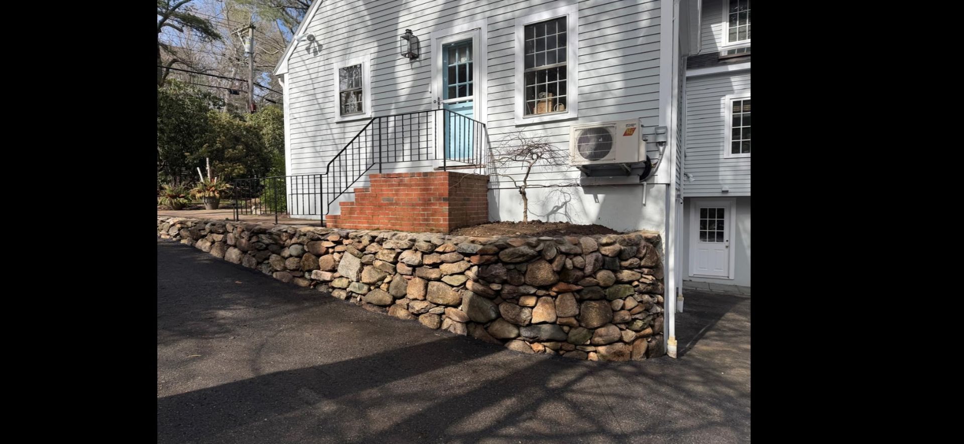 White house with stone retaining wall and brick steps beside a driveway in sunlight