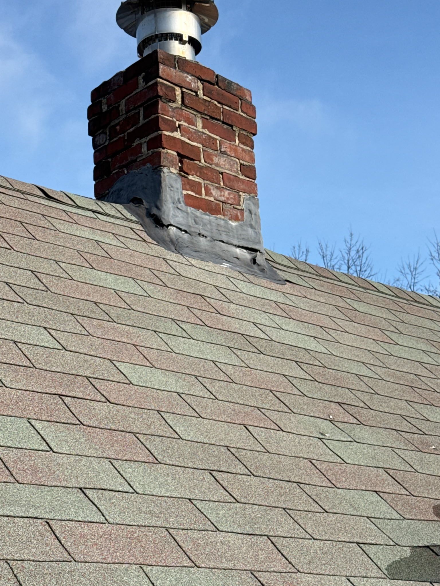 Brick chimney on a shingled roof against a blue sky.