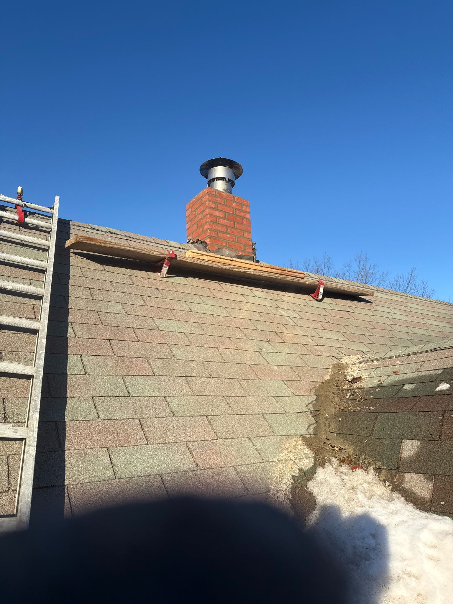 Stone wall and brick chimney under a clear blue sky, with a shadowed foreground.