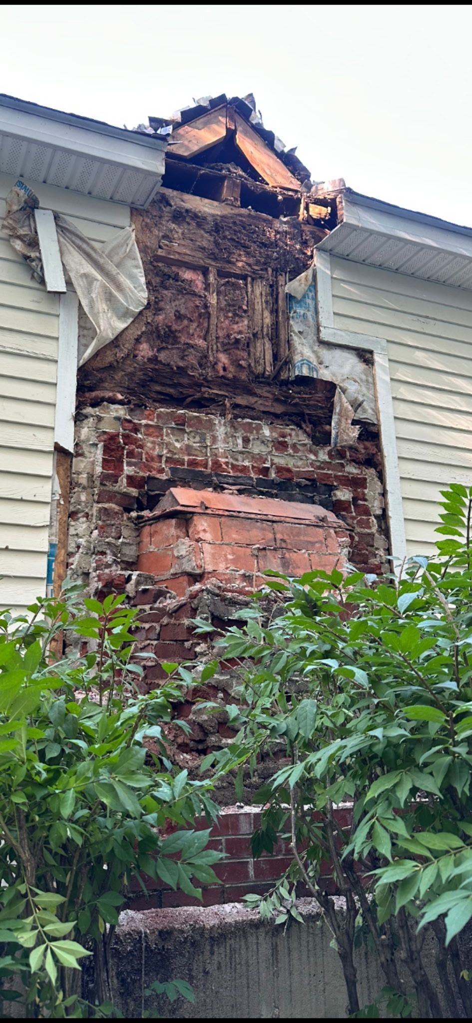 Damaged brick chimney on a house with missing bricks and exposed interior under the roofline
