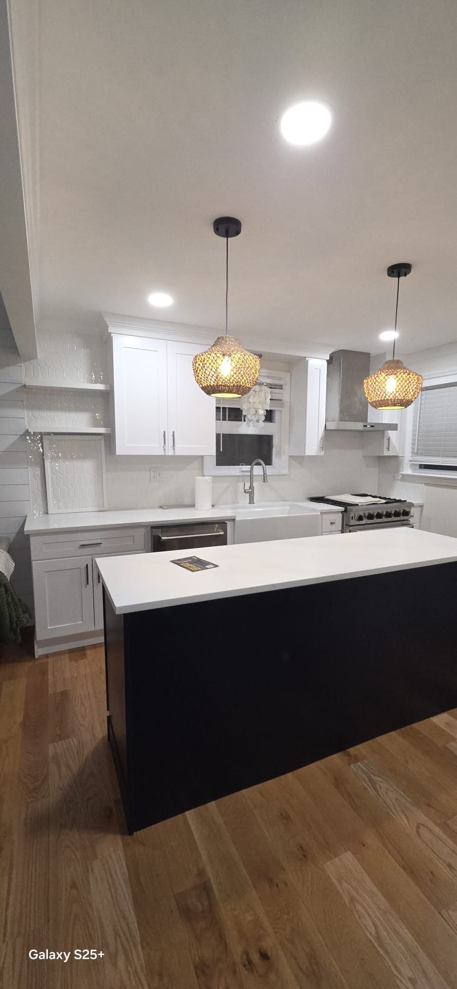 Modern white kitchen with black island, pendant lights, and hardwood floors