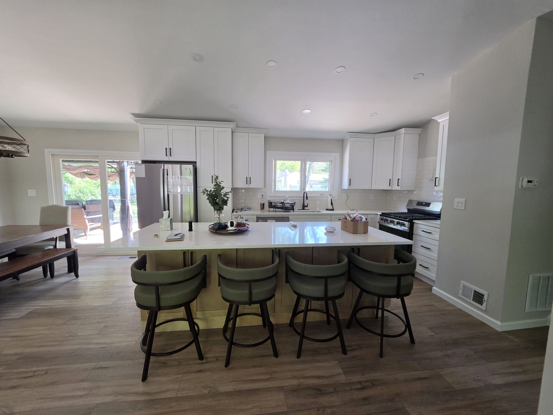 Bright open kitchen with white cabinets, island seating, stainless fridge, and sliding glass doors.