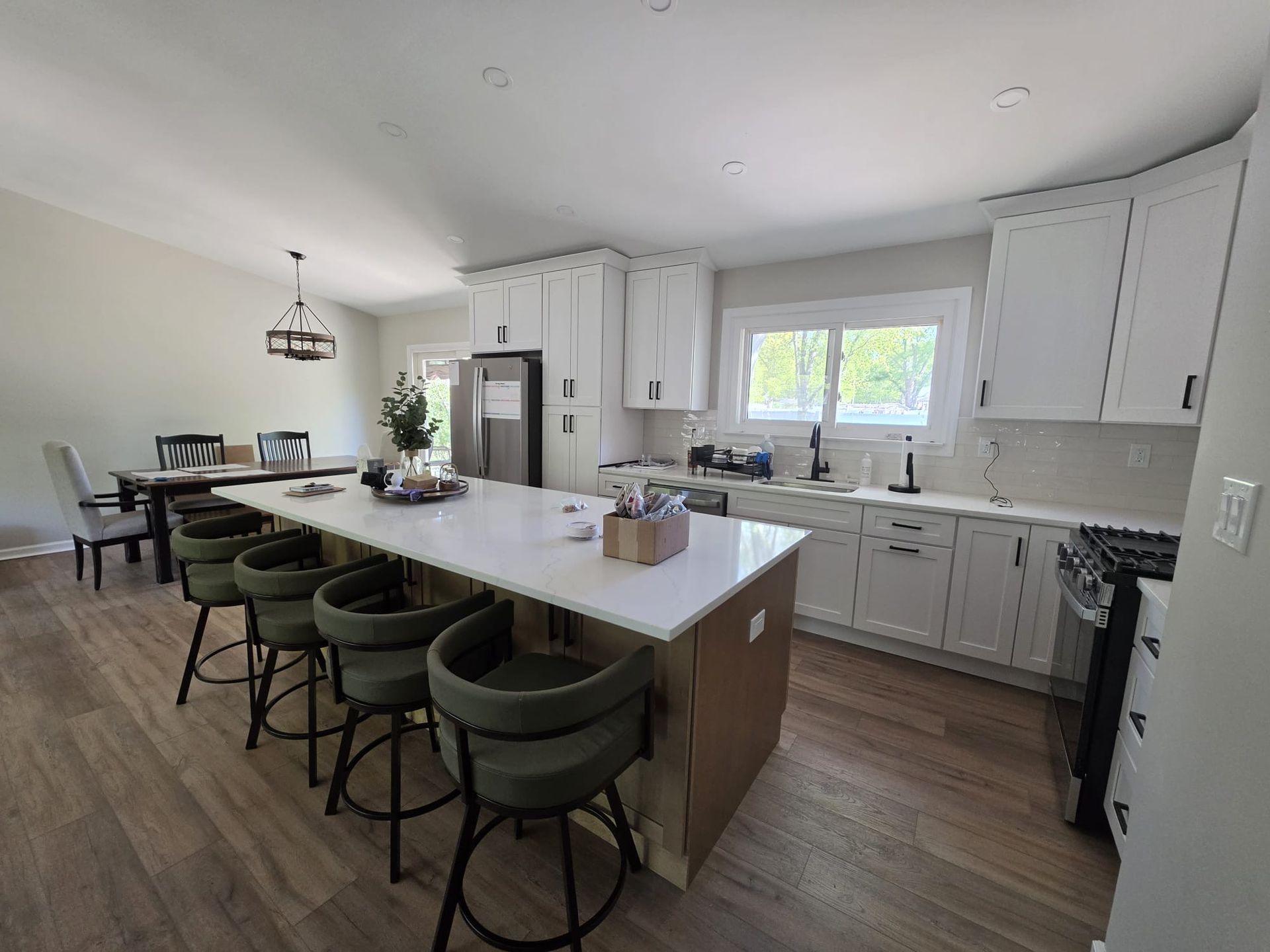 Modern kitchen with white cabinets, large island, green bar stools, and dining table in the background