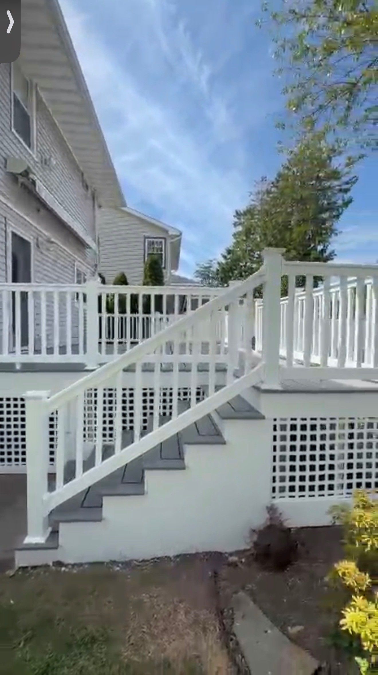 White house porch with raised deck, stairs, and white railings in a landscaped yard