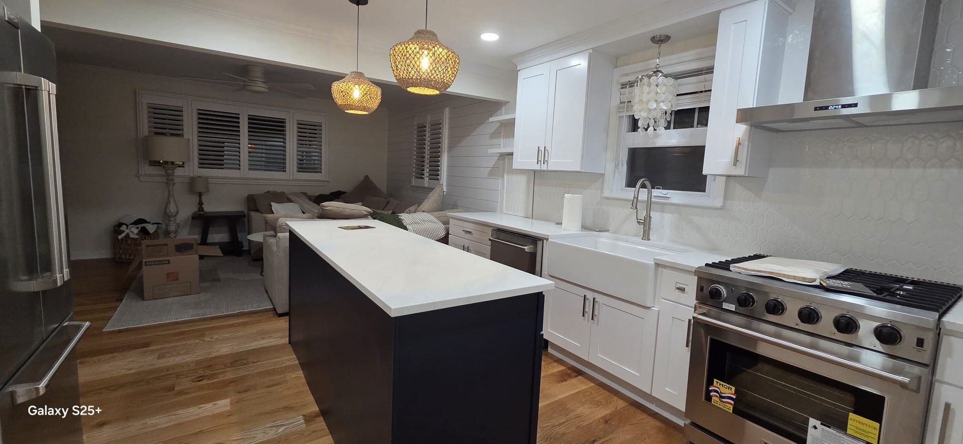 Modern white kitchen with island, pendant lights, stainless stove, and hardwood floors