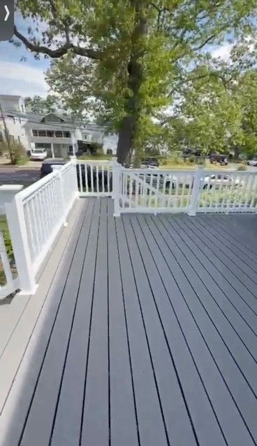 White-railed deck with gray flooring overlooking a tree-filled yard and a house
