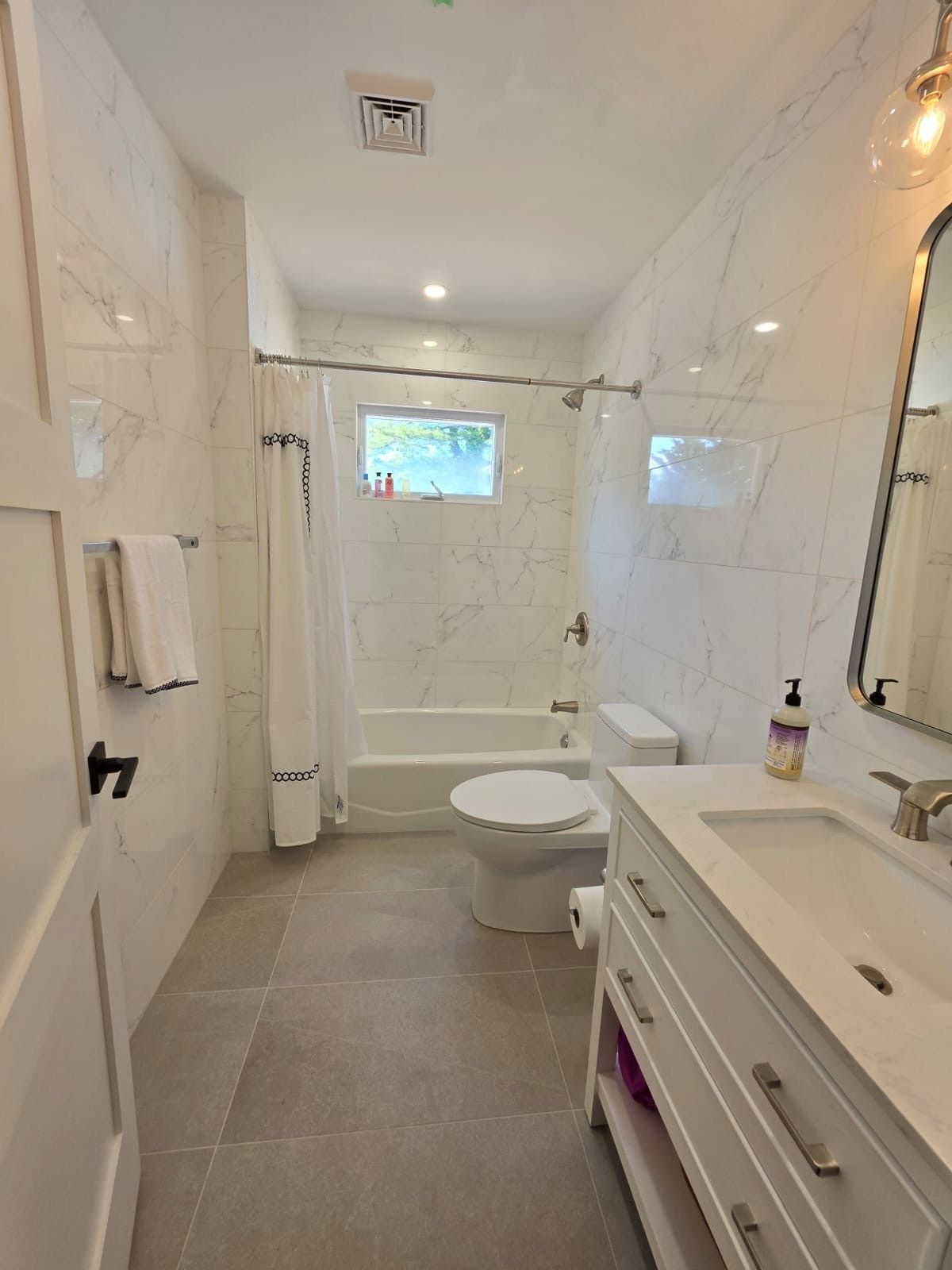 Bright white bathroom with walk-in shower, toilet, sink vanity, and tiled floor.