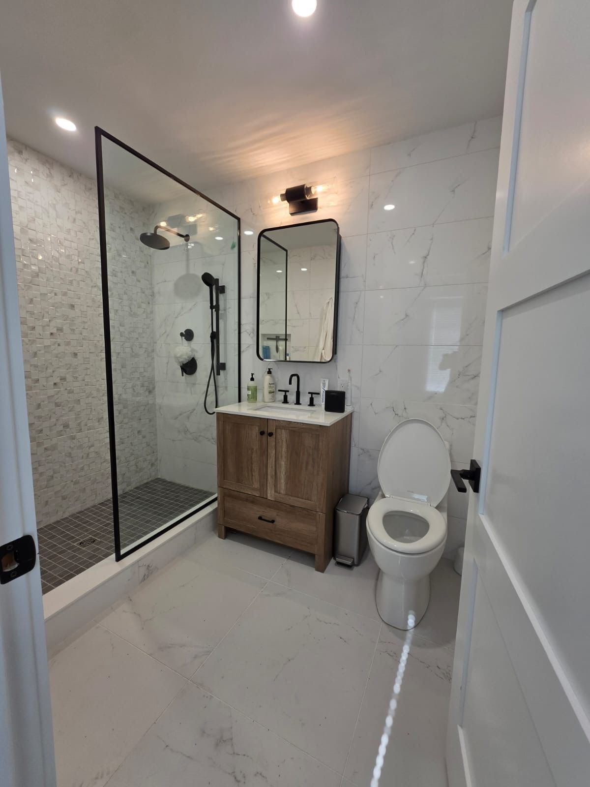 Bright white bathroom with a walk-in shower, toilet, sink, and vanity cabinet.