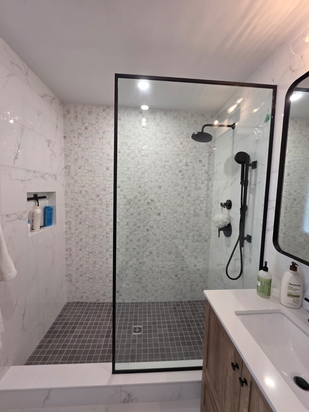 Modern white bathroom with glass shower, wooden vanity, mirror, and toilet.