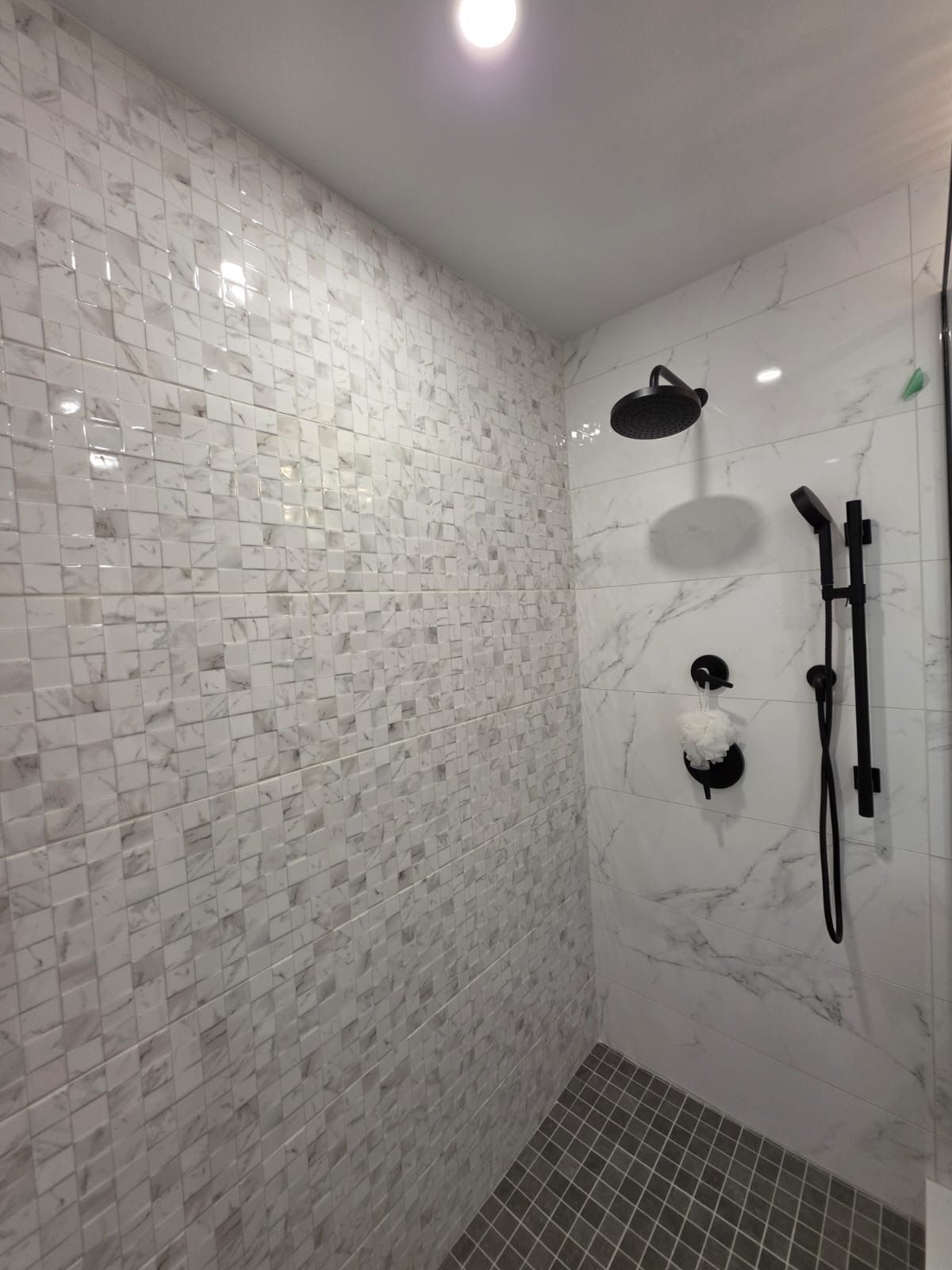 Small white-tiled shower with black fixtures and gray pebble floor in a bathroom.