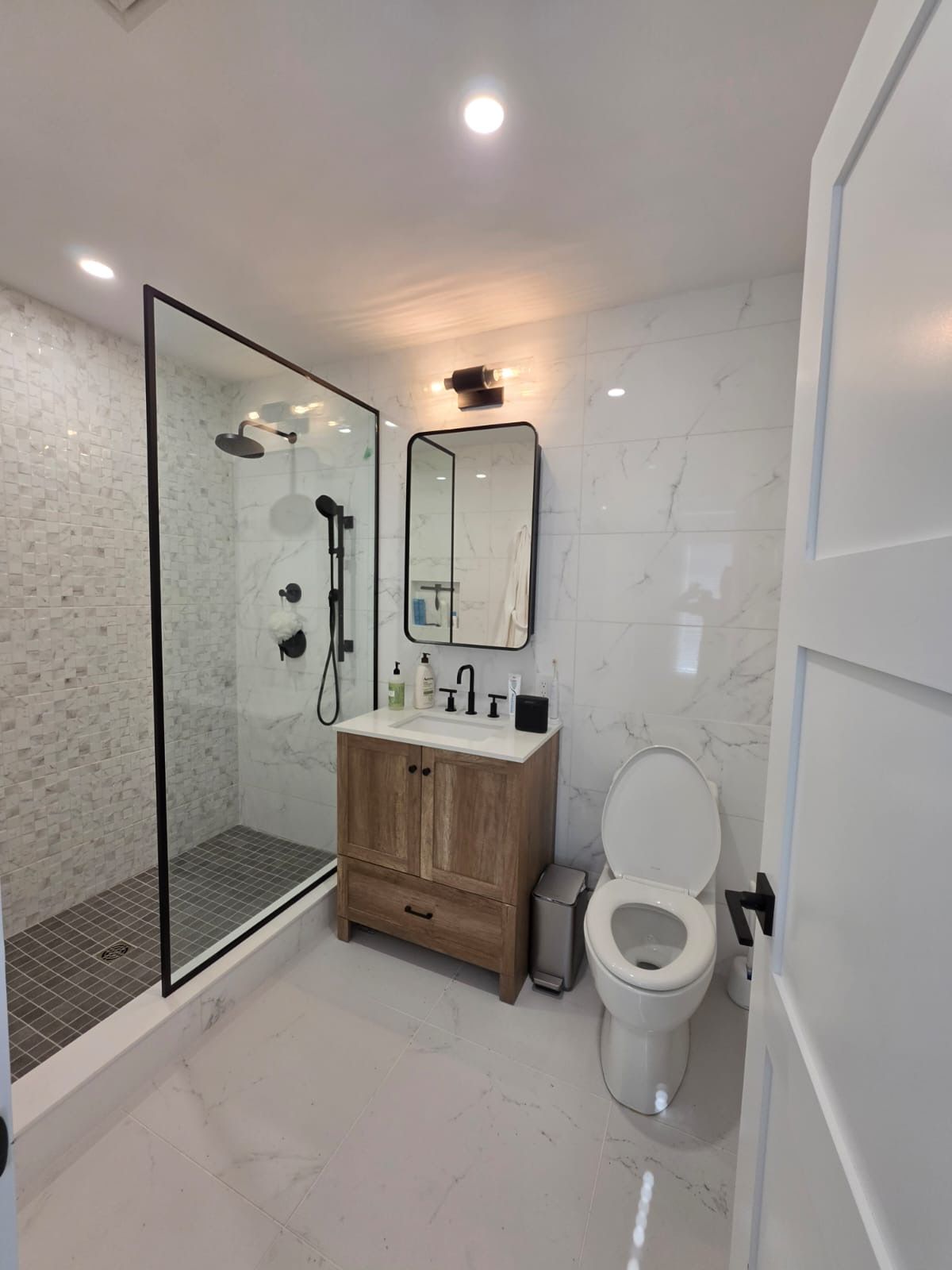 Modern bathroom with white tile, glass shower enclosure, and a dark wood vanity sink.