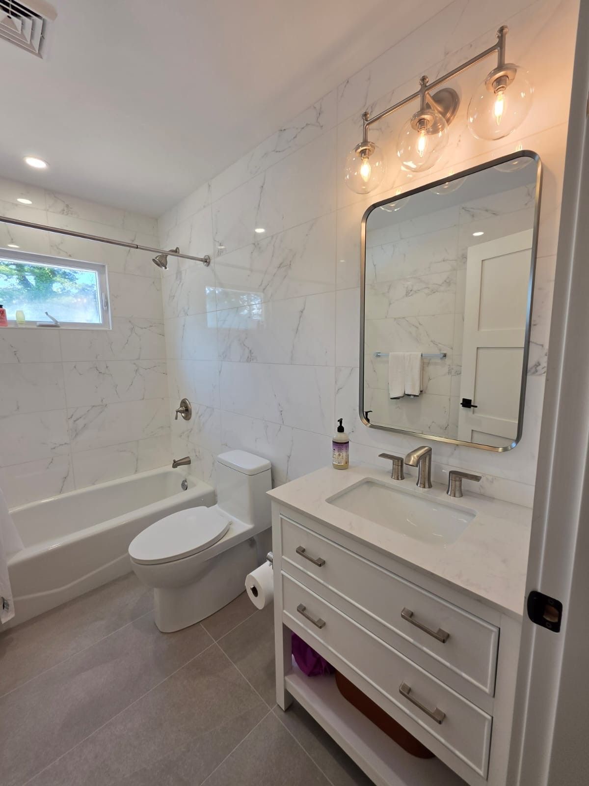 Modern tiled shower with black fixtures, white marble-look walls, and a pebble floor accent.