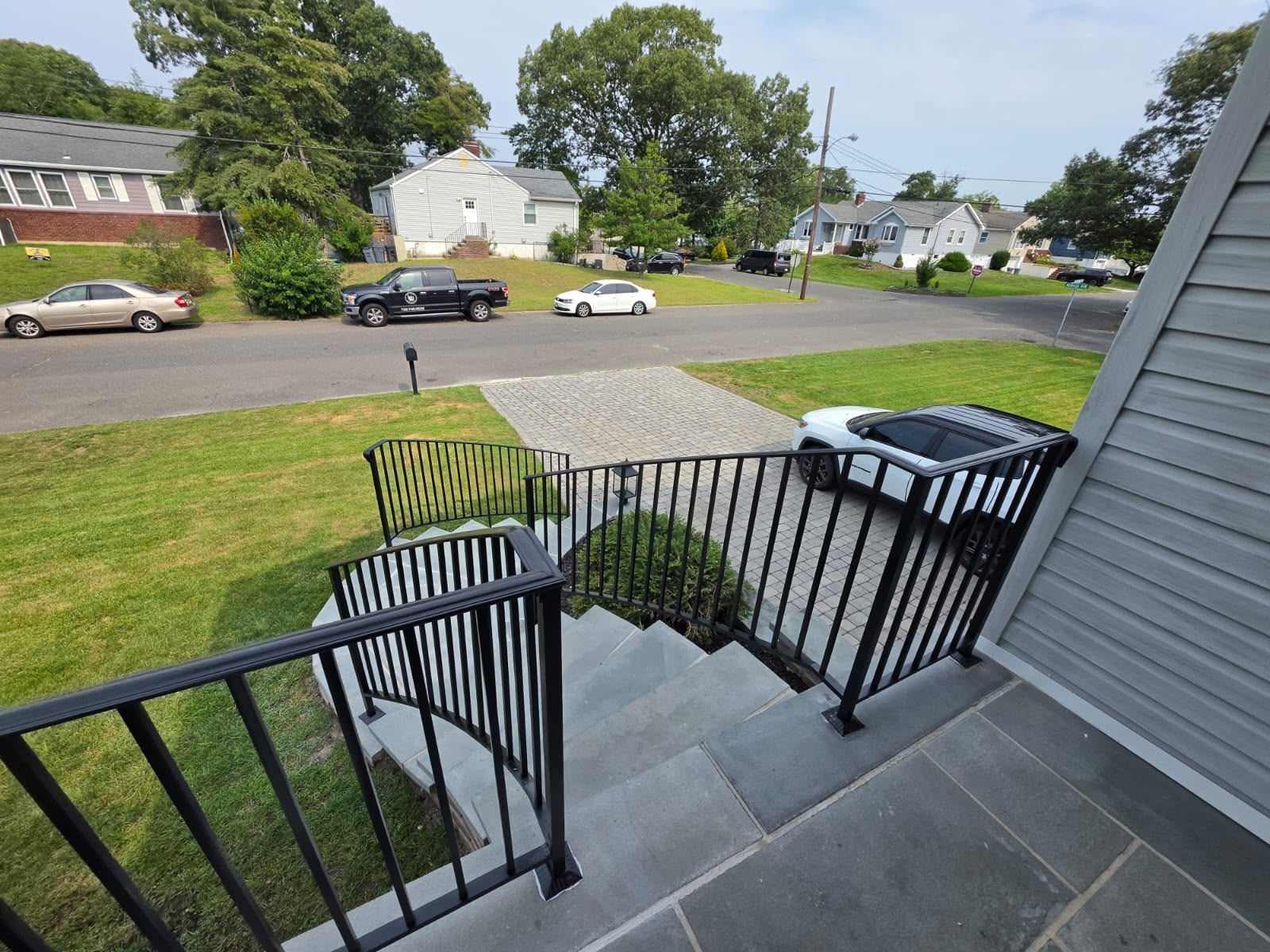 Front porch steps with black railings overlooking a quiet residential street and green lawn