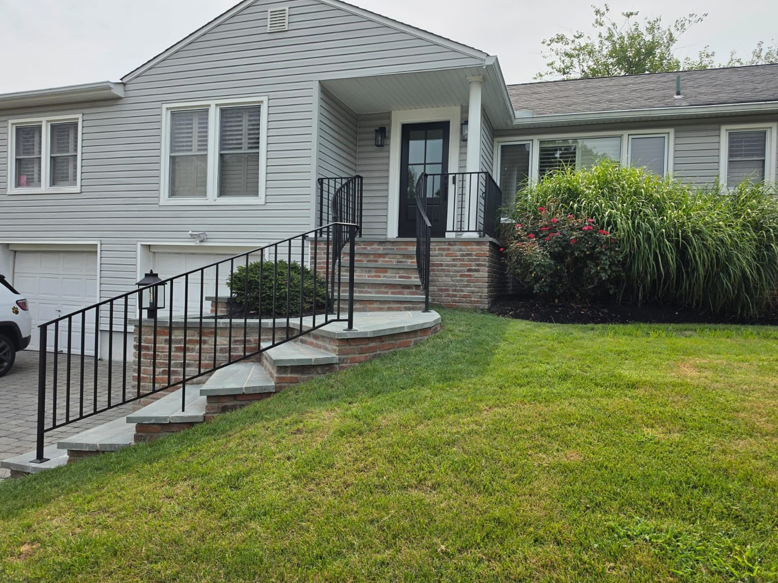 Gray house exterior with front steps, black railings, and a green lawn