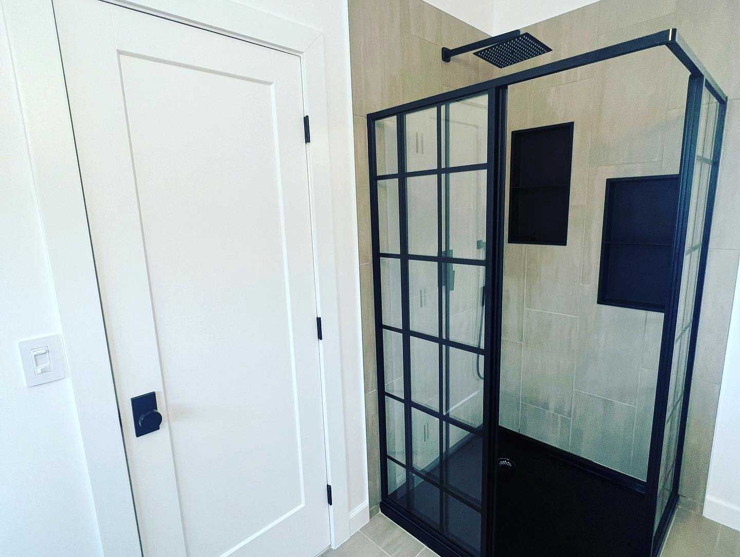 A bathroom with a black shower stall and a white door.