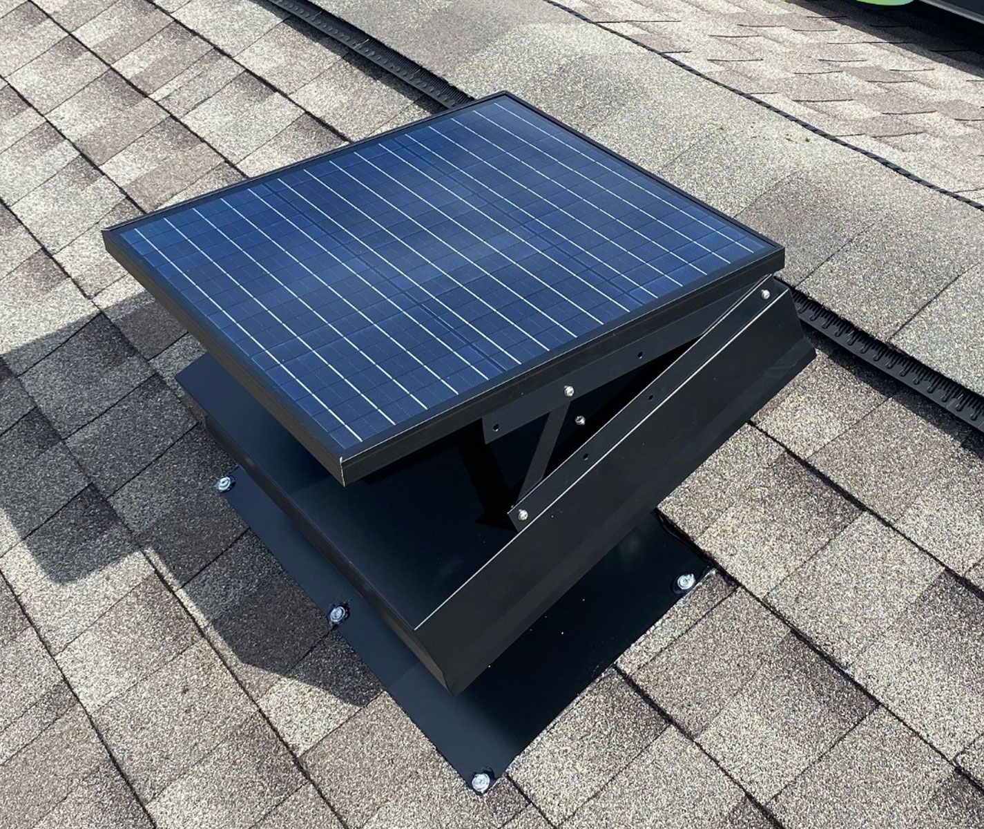 Solar-powered roof vent on a shingled roof, angled to face the sun. The vent is black with a blue solar panel.