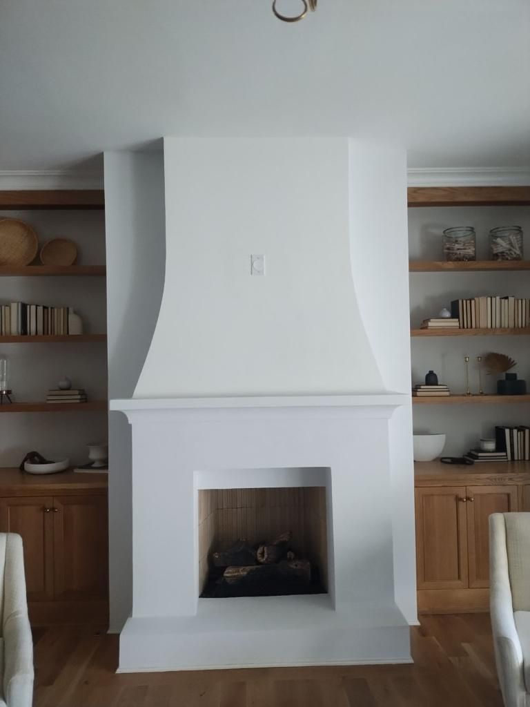 A white fireplace in a living room with a c on the wall above it
