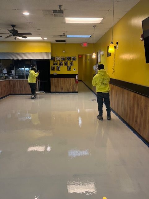 A man in a yellow hoodie is cleaning the floor of a restaurant