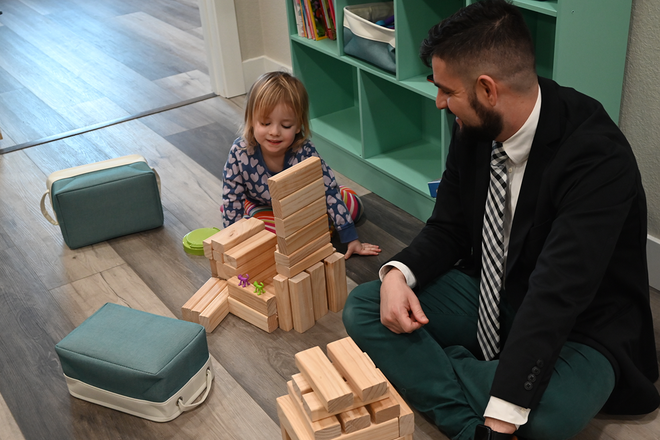 A person in a green dress speaks with two others sitting together on a couch in a bright office.