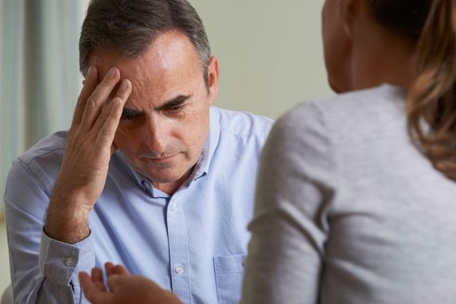 A distressed person rests their head in their hand while listening to someone sitting across from them.