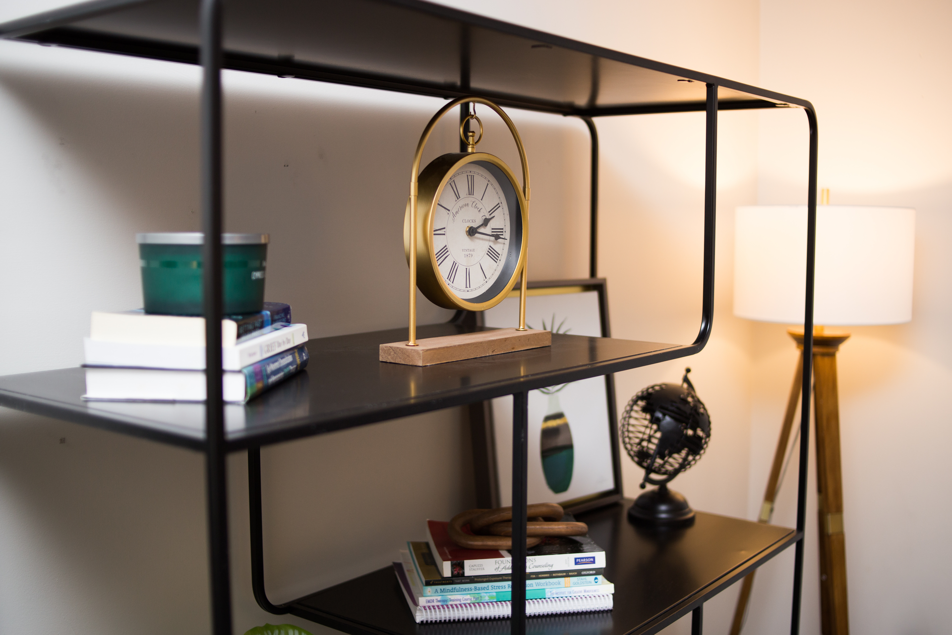 Black metal shelving unit with books, a clock, globe, and a lamp.