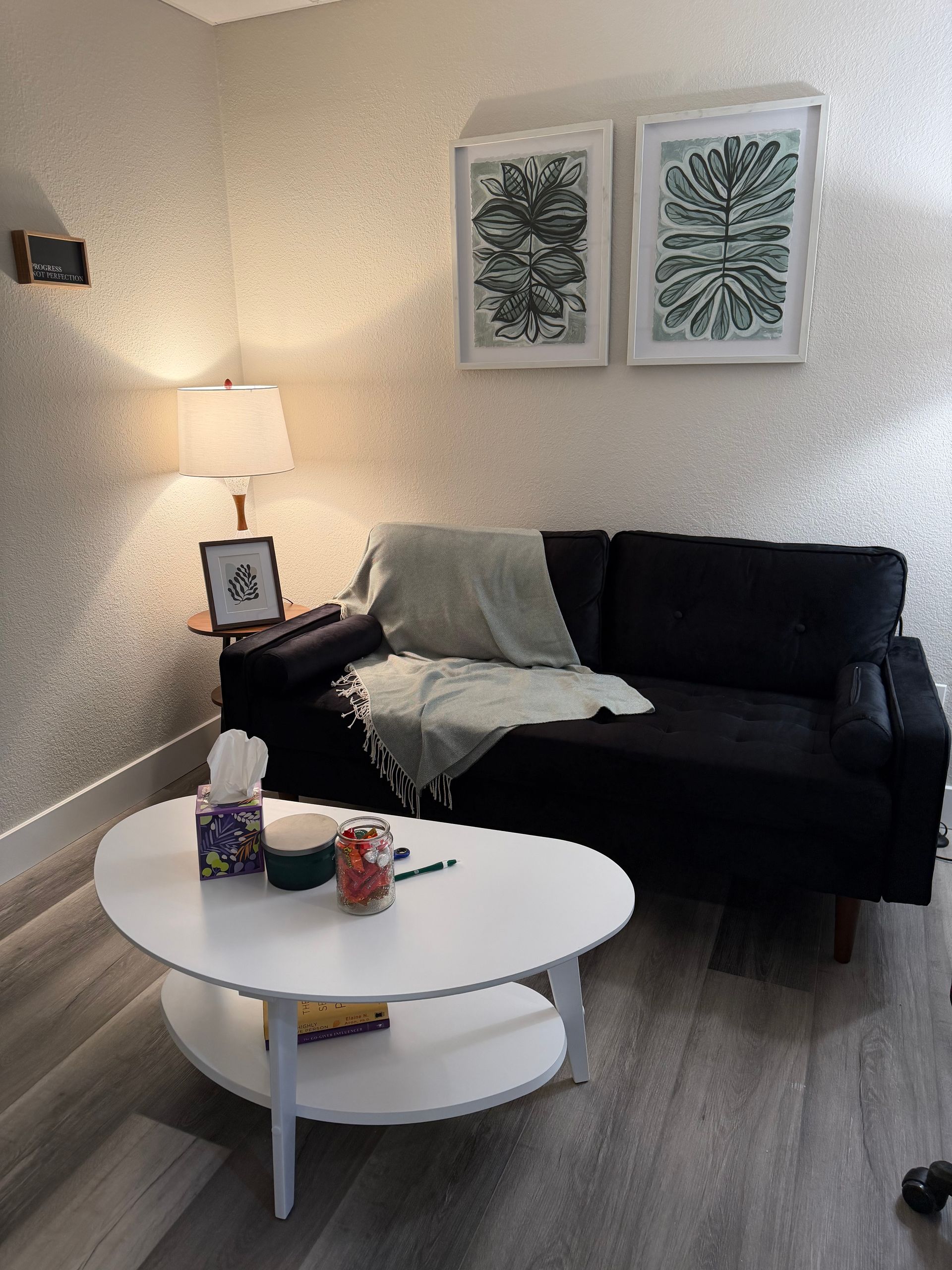A small, white coffee table sits before a black sofa with a light-colored throw blanket in a room with patterned walls.