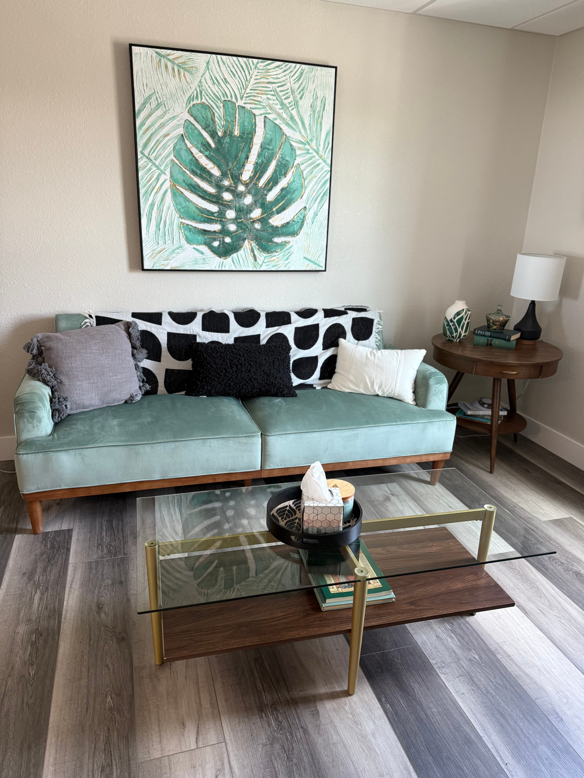 A mint green sofa with decorative pillows in a waiting room with a coffee table and art.
