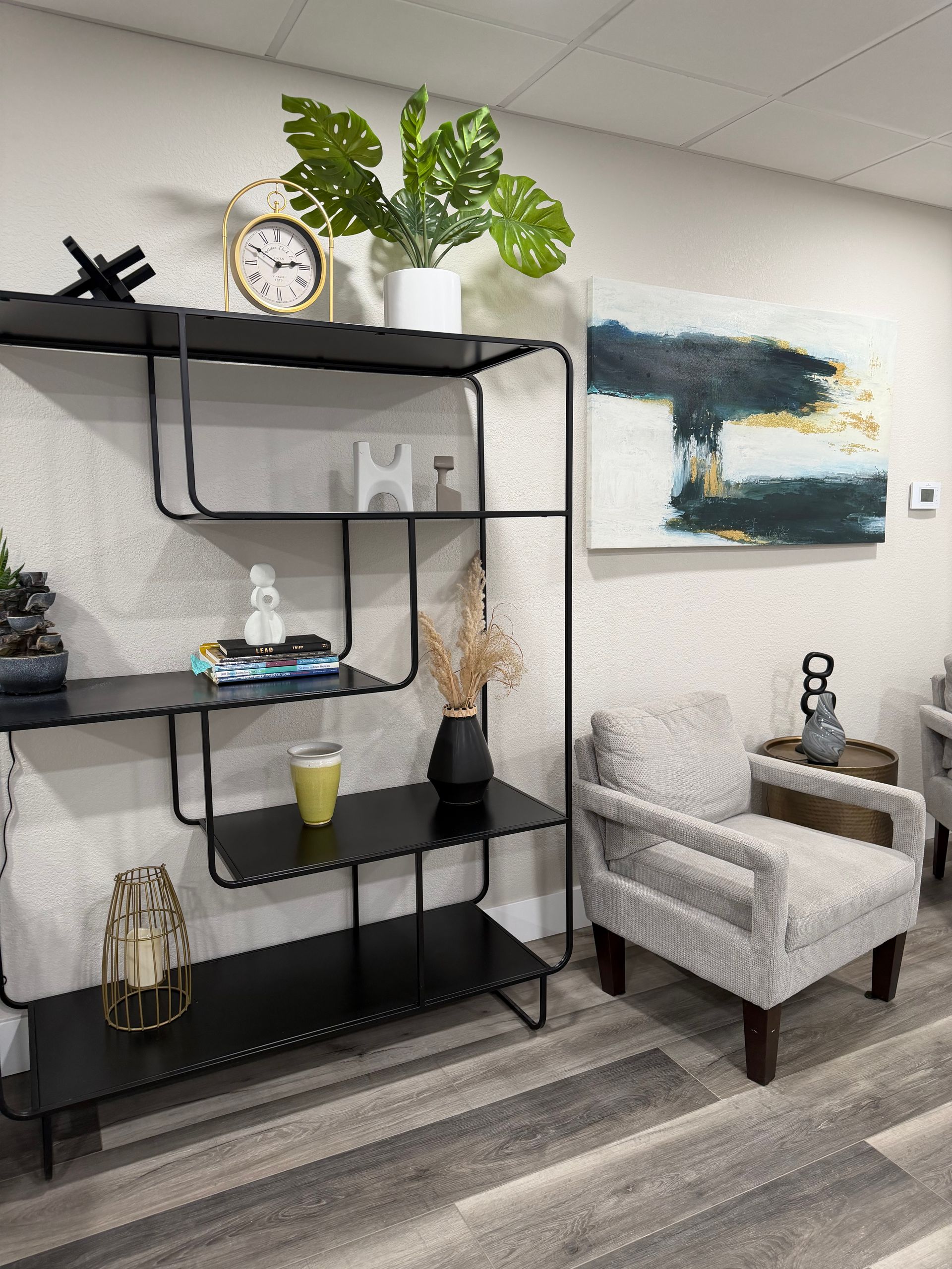 A modern room featuring a black tiered shelving unit decorated with plants and decor, next to a textured armchair.