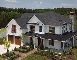 White farmhouse with black roof, brown garage doors, and a stone chimney.