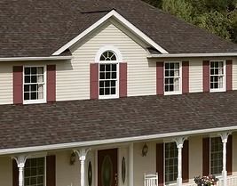 Two-story house with tan siding, burgundy shutters, and a dark brown shingle roof.