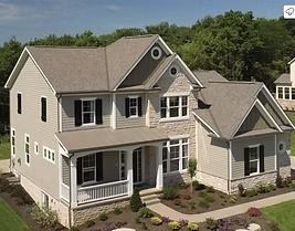 Two-story beige house with stone accents, covered porch, and black shutters, set among trees.