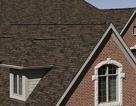 Brown shingle roof on a brick house with a white-framed window.